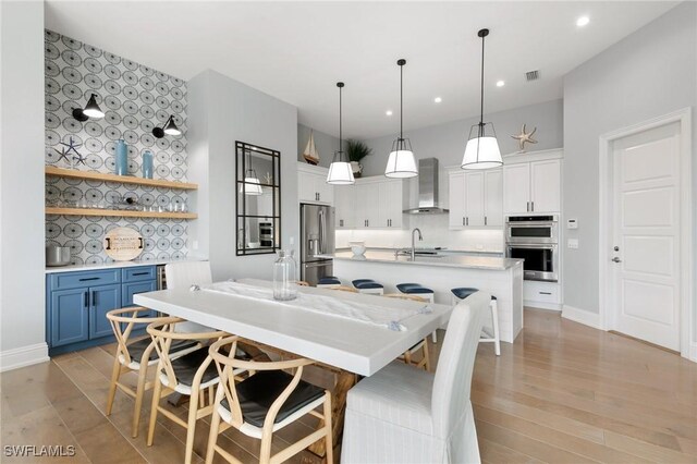 interior space with decorative light fixtures, white cabinets, stainless steel appliances, blue cabinetry, and wall chimney range hood