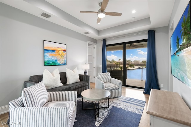 living room featuring ceiling fan, a raised ceiling, and light wood-type flooring