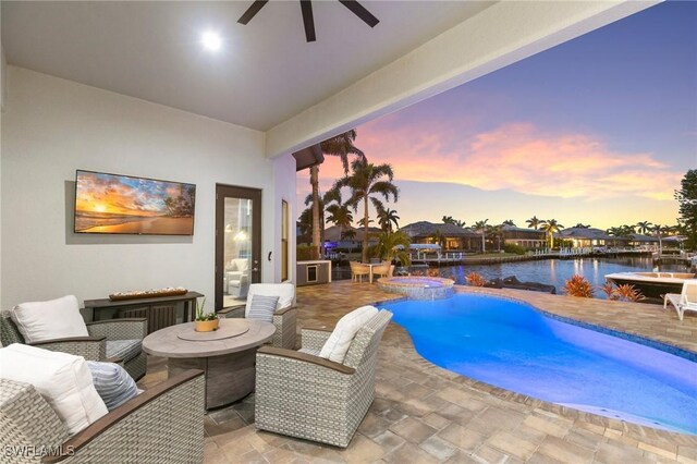 pool at dusk with an in ground hot tub, a water view, ceiling fan, and a patio