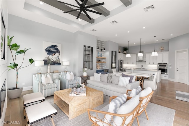 living room with light wood-type flooring, ceiling fan, sink, and a high ceiling