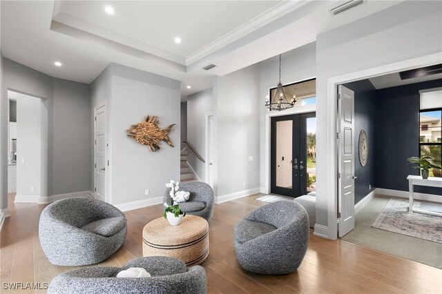 sitting room with wood-type flooring, a notable chandelier, crown molding, and a tray ceiling