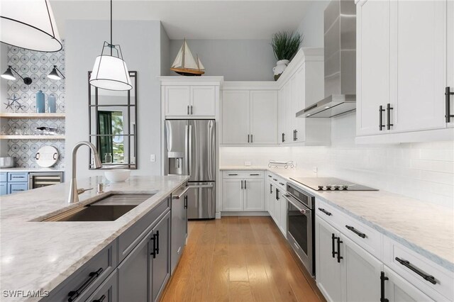 kitchen featuring appliances with stainless steel finishes, white cabinetry, sink, light stone counters, and wall chimney exhaust hood