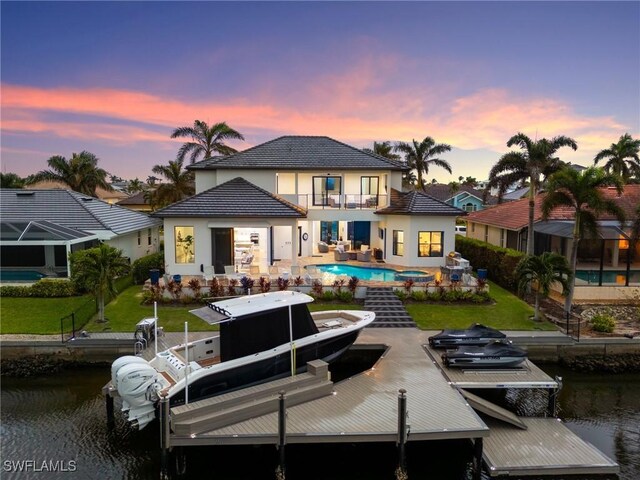 back house at dusk featuring a patio, a balcony, and a water view