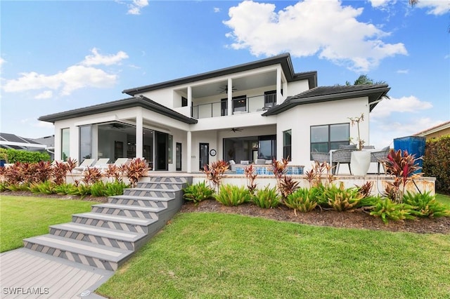 back of house featuring ceiling fan, a balcony, and a lawn