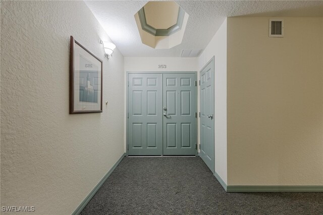 hallway featuring a textured ceiling and dark colored carpet