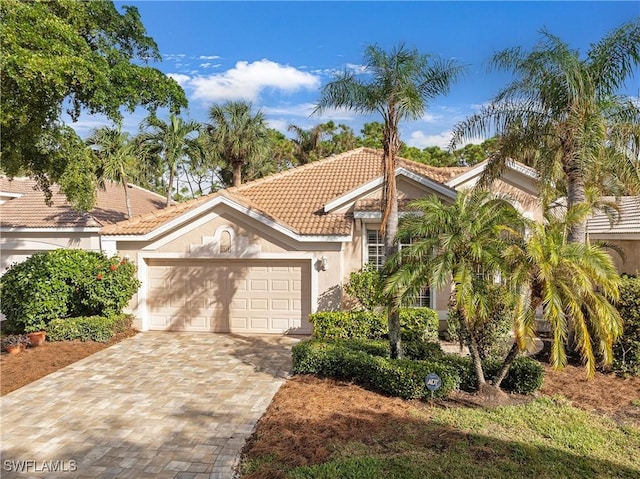 mediterranean / spanish-style house with decorative driveway, an attached garage, a tile roof, and stucco siding