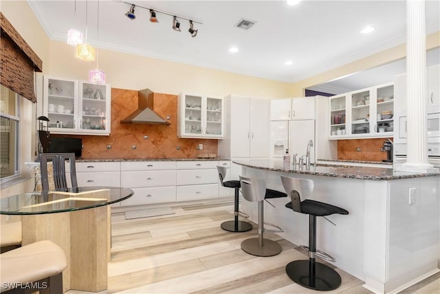 kitchen featuring wall chimney range hood, decorative backsplash, a kitchen bar, visible vents, and ornamental molding