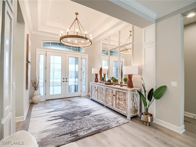 foyer featuring a notable chandelier, french doors, light wood-type flooring, and a raised ceiling