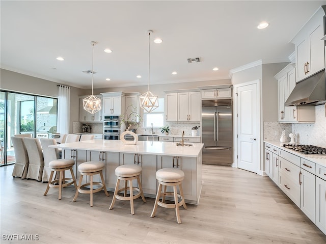 kitchen featuring light wood-type flooring, an island with sink, a kitchen breakfast bar, hanging light fixtures, and stainless steel appliances