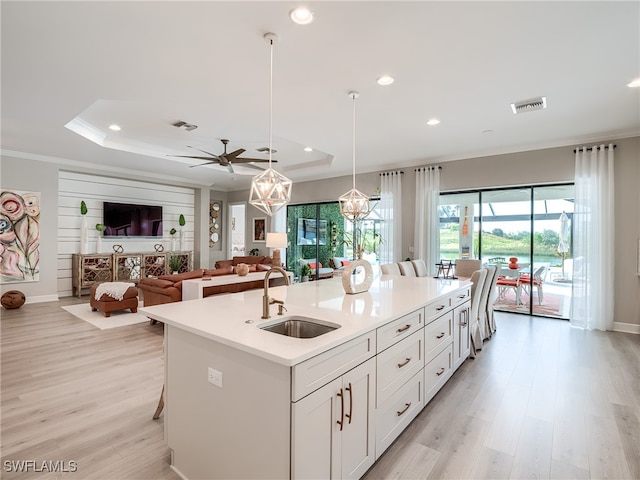 kitchen with a center island with sink, sink, decorative light fixtures, white cabinetry, and light hardwood / wood-style floors