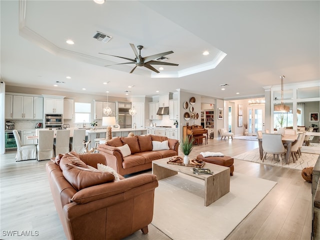 living room with crown molding, light hardwood / wood-style flooring, a raised ceiling, and ceiling fan