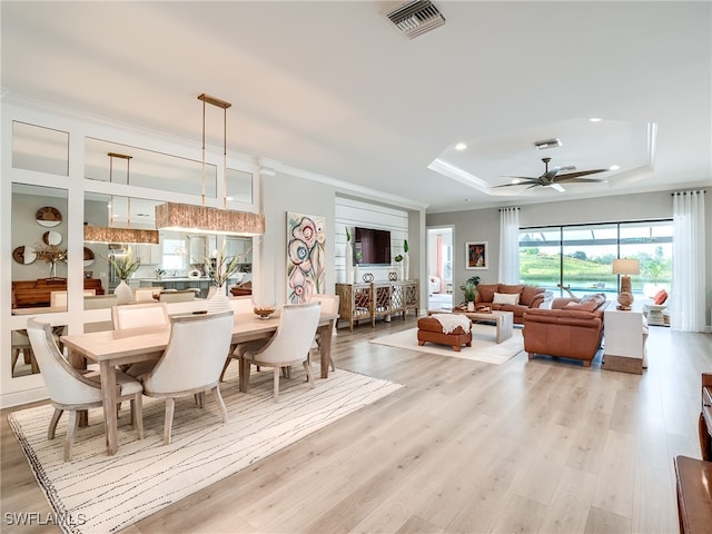 dining room featuring ceiling fan, ornamental molding, a tray ceiling, and light wood-type flooring