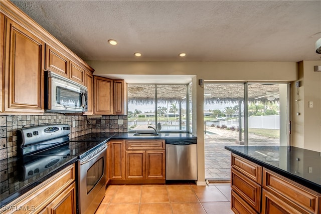 kitchen with appliances with stainless steel finishes, sink, dark stone countertops, decorative backsplash, and light tile patterned floors