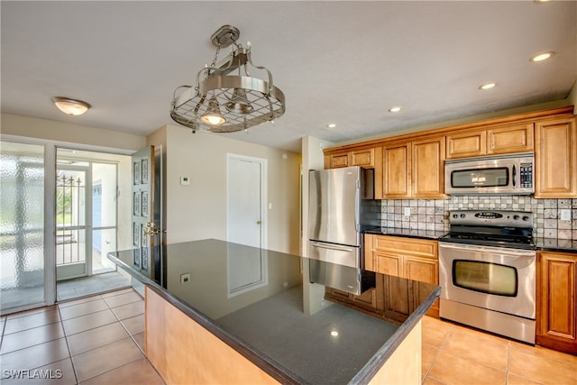 kitchen featuring decorative backsplash, stainless steel appliances, dark stone counters, a center island, and light tile patterned flooring