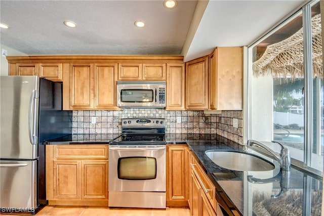 kitchen with sink, backsplash, stainless steel appliances, dark stone counters, and light tile patterned floors