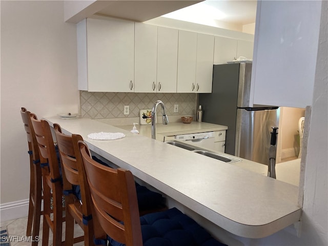 kitchen featuring a breakfast bar area, light countertops, decorative backsplash, white cabinets, and a peninsula