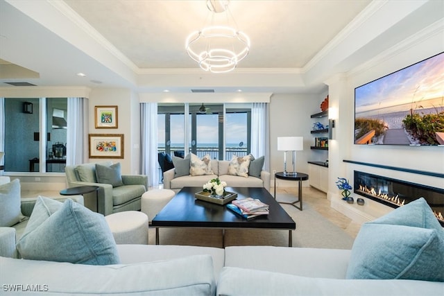 living room featuring a tray ceiling, a water view, a chandelier, and crown molding