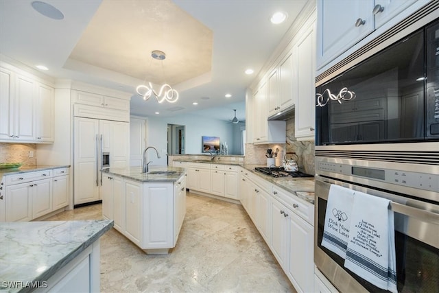 kitchen featuring built in appliances, white cabinets, sink, a raised ceiling, and decorative light fixtures