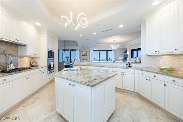 kitchen with stainless steel appliances, white cabinetry, a raised ceiling, pendant lighting, and an island with sink