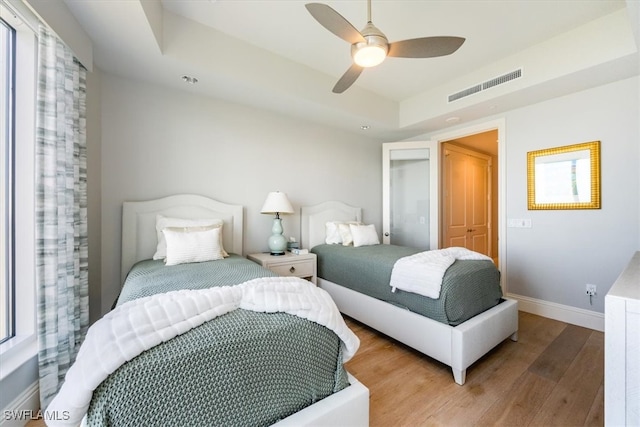 bedroom with hardwood / wood-style floors, ceiling fan, a closet, and a raised ceiling