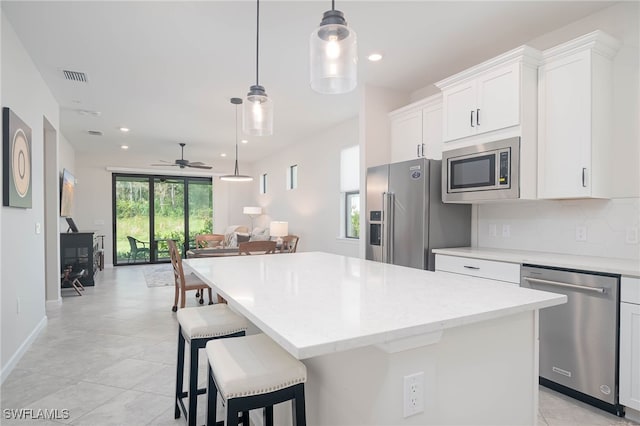 kitchen with ceiling fan, appliances with stainless steel finishes, white cabinetry, decorative light fixtures, and a center island