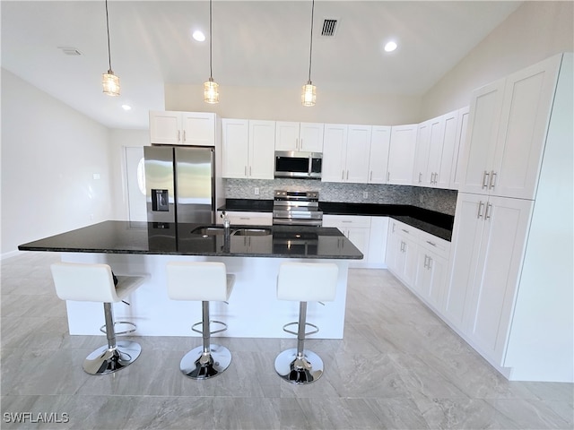 kitchen featuring white cabinets, appliances with stainless steel finishes, a breakfast bar, and an island with sink