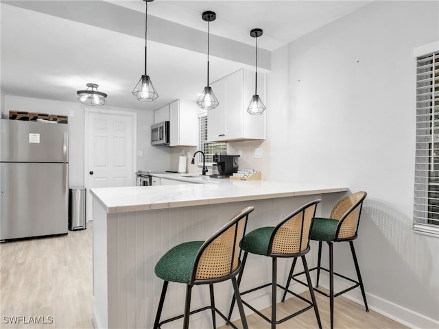 kitchen with appliances with stainless steel finishes, a kitchen bar, kitchen peninsula, white cabinets, and light hardwood / wood-style flooring