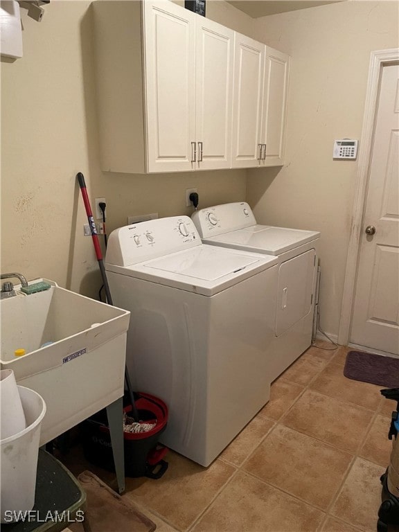 clothes washing area with sink, washing machine and clothes dryer, light tile patterned floors, and cabinets