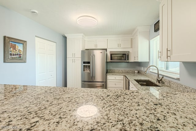 kitchen with appliances with stainless steel finishes, white cabinets, light stone countertops, and sink