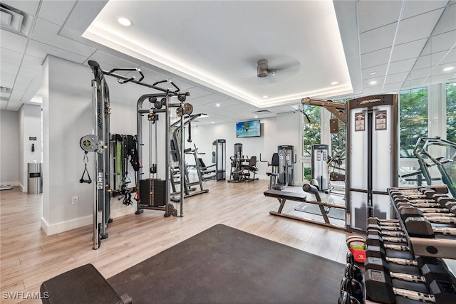 exercise room featuring floor to ceiling windows, wood-type flooring, a raised ceiling, and ceiling fan