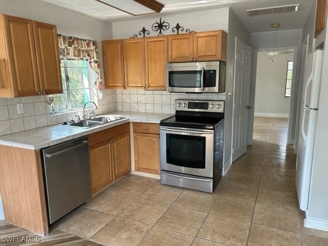 kitchen with sink, stainless steel appliances, tile counters, and tasteful backsplash