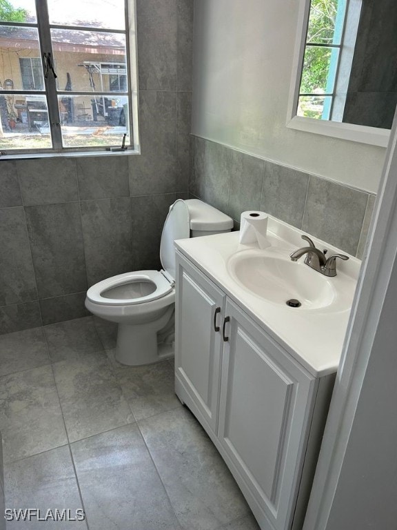 bathroom with tile walls, vanity, toilet, and tile patterned floors