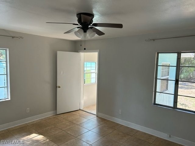 empty room with a wealth of natural light, light tile patterned floors, and ceiling fan