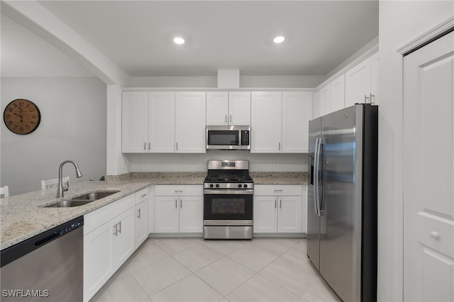 kitchen with kitchen peninsula, white cabinets, light stone counters, appliances with stainless steel finishes, and sink