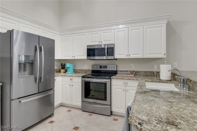 kitchen with light stone countertops, appliances with stainless steel finishes, sink, light tile patterned floors, and white cabinets