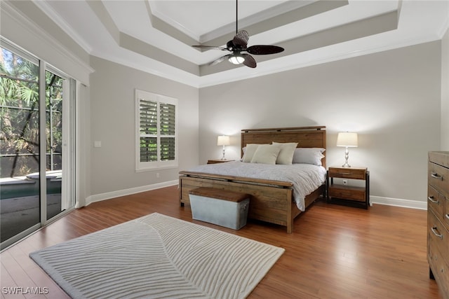 bedroom featuring access to exterior, ceiling fan, wood-type flooring, a tray ceiling, and ornamental molding