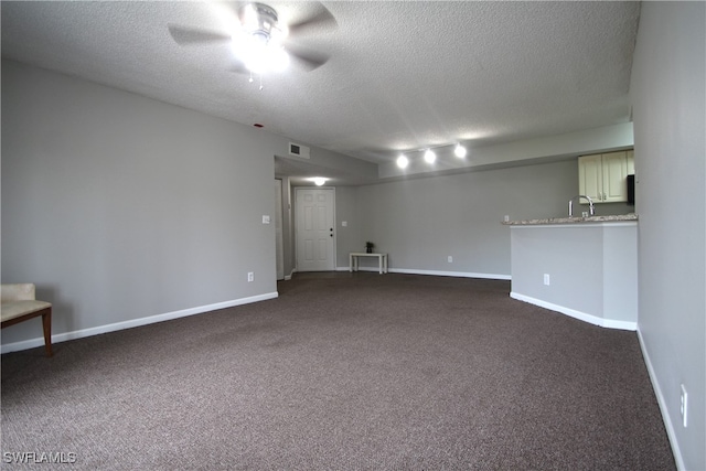 unfurnished room with ceiling fan, a textured ceiling, and dark colored carpet