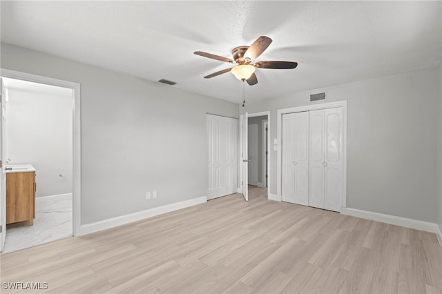 unfurnished bedroom with two closets, a textured ceiling, light hardwood / wood-style floors, and ceiling fan