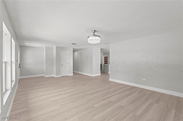 unfurnished living room featuring brick wall, a textured ceiling, and light hardwood / wood-style flooring