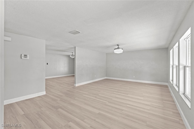 empty room with light hardwood / wood-style flooring, a notable chandelier, and a textured ceiling