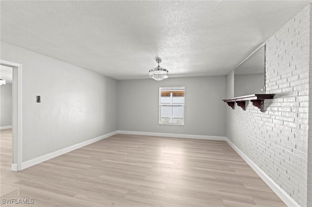 spare room featuring light hardwood / wood-style flooring, a textured ceiling, a notable chandelier, and brick wall