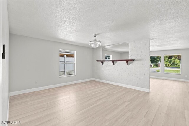 unfurnished living room featuring light hardwood / wood-style floors, brick wall, a textured ceiling, and a chandelier