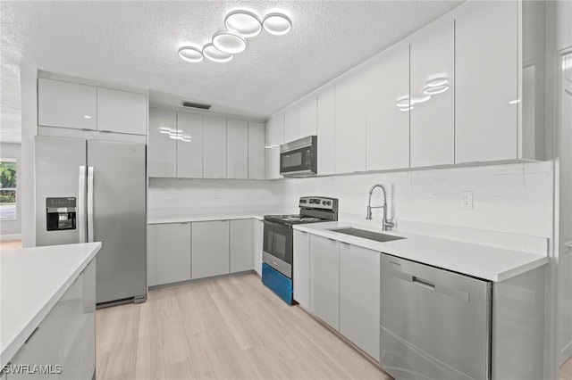 kitchen with light hardwood / wood-style flooring, stainless steel appliances, a textured ceiling, and sink