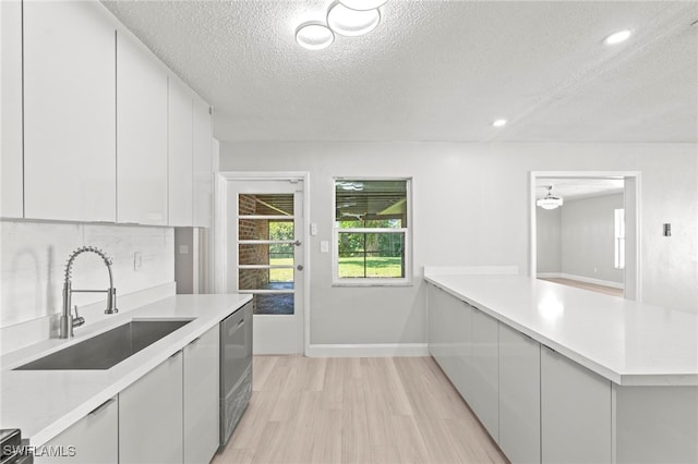 kitchen with dishwasher, sink, light wood-type flooring, a textured ceiling, and white cabinets