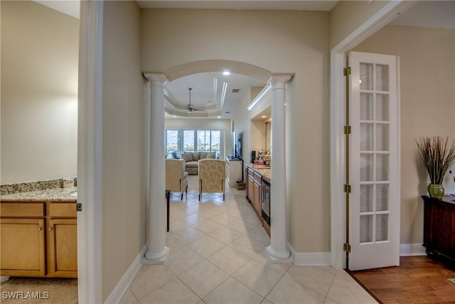 corridor featuring baseboards, arched walkways, light tile patterned floors, decorative columns, and a raised ceiling