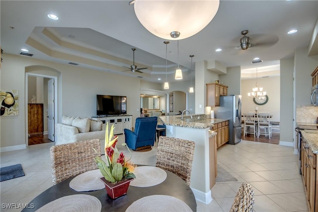 dining room with light tile patterned floors, a tray ceiling, recessed lighting, arched walkways, and ceiling fan with notable chandelier