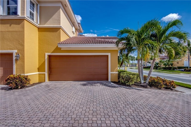 exterior space with a tiled roof, decorative driveway, an attached garage, and stucco siding