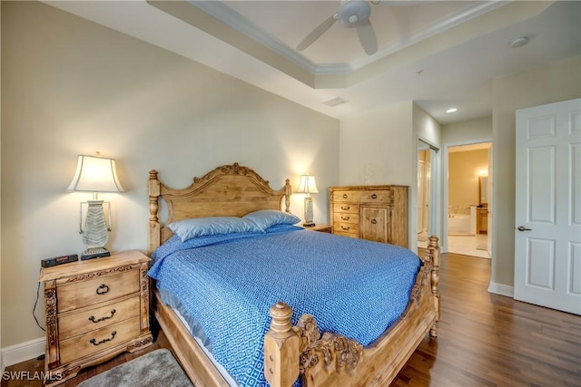 bedroom with ensuite bath, a raised ceiling, dark wood-style floors, and baseboards