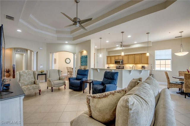 living room with visible vents, ornamental molding, arched walkways, a raised ceiling, and ceiling fan