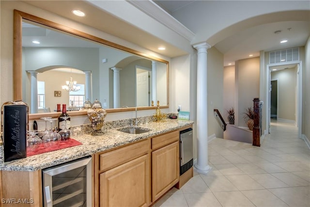 kitchen featuring beverage cooler, light brown cabinets, ornate columns, and a sink